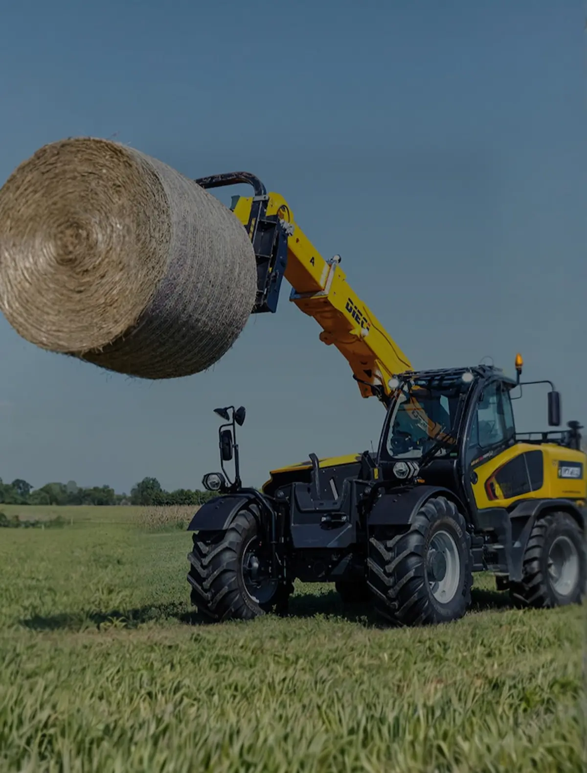 Încărcător telescopic second hand ridicând un balot mare de paie pe câmp agricol